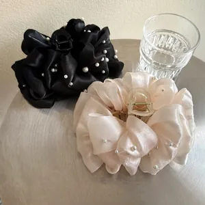 Dettaglio di grandi mollette per capelli in raso nero e champagne con perle bianche