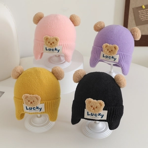 Detailed knit texture of toddler earflap hats with fluffy pom-poms and bear patch