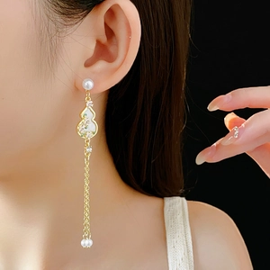 Detail of long gold gourd earrings with enamel flowers and faux pearl tassels