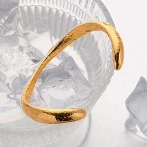 Irregular 18k gold plated stainless steel open bangle on ice cubes in a glass