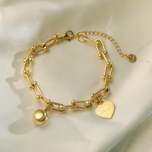 Golden stainless steel U-link bracelet with heart and ball charms on white silk fabric