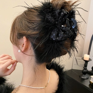 Detail of large black hair claw clip with feathers and sequins worn on a messy bun