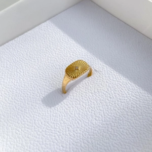 Detail of gold sunburst signet ring with a central diamond on a white leather base