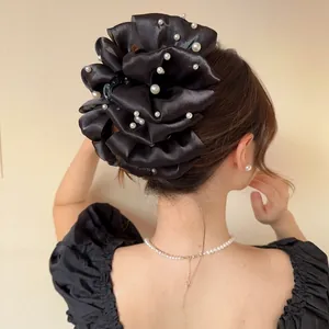 Dettaglio macro di un grande fermaglio per capelli in raso nero con eleganti perle bianche