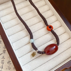 Macro shot of wax cord necklace with red agate beads and vintage engraved metal pendant