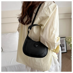 Detail of black leather half-moon shoulder bag with minimalist heart relief decoration