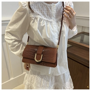 Détail du sac marron foncé effet crocodile avec boucle dorée porté par un mannequin