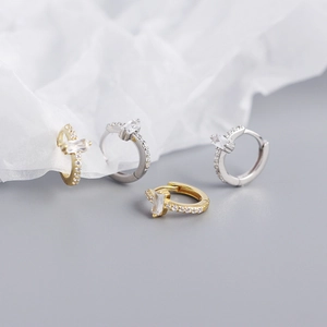 Macro detail of gold and silver rectangular zircon earrings on minimalist textured paper