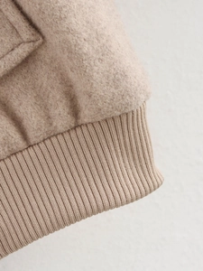 Detailed macro view of the ribbed hem and soft wool texture on a beige tweed jacket
