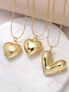 Three gold heart pendants showing smooth, puffy, and engraved details on marble surface