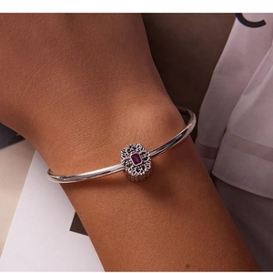 Macro shot of silver charm bracelet featuring a red rectangular gemstone and filigree