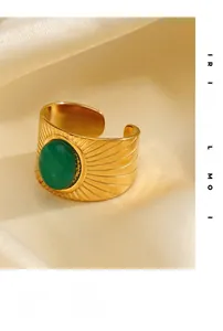 Close-up of a wide gold-plated ring with a green stone and radiating sunray texture