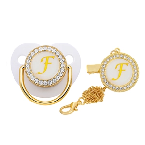 Detail of white baby pacifier with gold letter F and rhinestone accents with clip chain