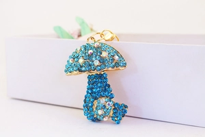 Close-up of golden mushroom keychain charm with pavé blue rhinestones on white background