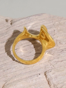 Macro detail of gold-plated wavy geometric ring resting on natural stone block