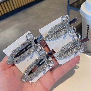 Silver bow hair clips with rhinestones and pearls shown in a stylish hand-held view