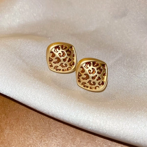 Detail shot of leopard print hollow square earrings on elegant beige silk fabric