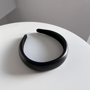 Close-up of a chic black PU leather headband on a minimalist white surface