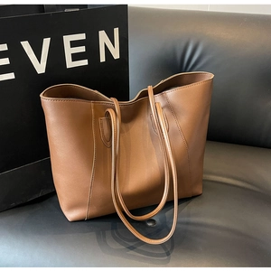 Close-up of a large brown leather tote bag on a black sofa with soft natural lighting