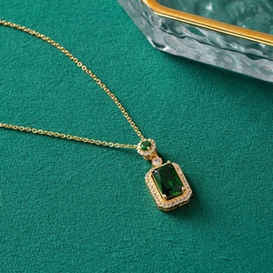 Detail of emerald cut green pendant necklace with diamond halo on dark green fabric