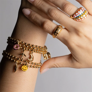 Gold beaded bracelets and enamel rings set featuring pink donut and plane charms