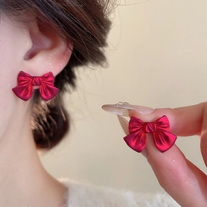 Detail view of dark red bow stud earrings with matte metal finish and 3D textured design