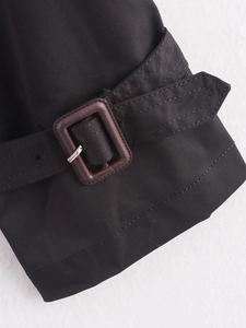 Close-up of black trench coat sleeve strap with textured fabric and resin buckle detail
