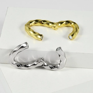 Twisted magnetic hoop earrings in gold and silver steel finish on a white pedestal