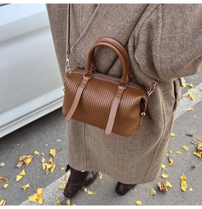 Close-up of brown Boston bag with vertical pleated texture and dual handles for autumn
