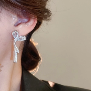 Close-up of sparkling bow tassel earrings with zircon crystals worn by a model