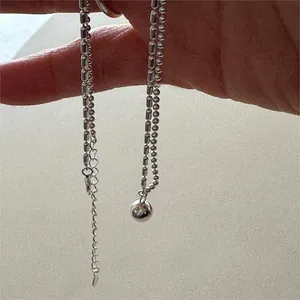 Detail of silver beaded ball chain necklace with round pendant held in hand