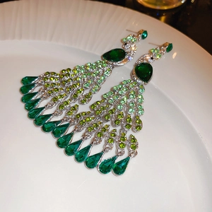 Detail view of peacock-shaped tassel earrings with emerald green crystals on white ceramic