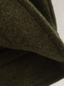 Gros plan du tissu en tweed vert foncé montrant la texture épaisse et les coutures