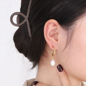 Gros plan d'une boucle d'oreille dorée 18K avec perle d'eau douce portée par une femme