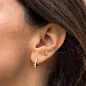 Detailed view of a gold snake earring and turquoise stud set worn on ear