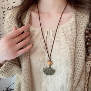 Detailed view of bronze ginkgo leaf pendant with wooden bead on vintage ethnic necklace