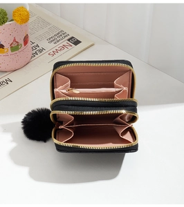Top view of compact black wallet with gold zipper, pink lining and fur pompom detail