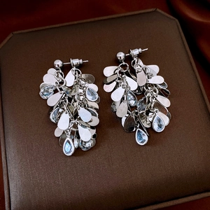 Macro detail of silver tassel earrings with water blue crystals on dark silk fabric