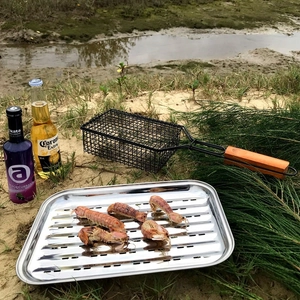 Outdoor stainless steel grilling pan with handles used on a beach during a camping trip