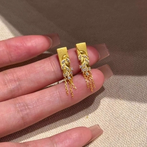 Detail of gold wheat leaf earrings with sparkling cubic zirconia tassels on linen