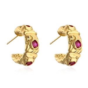 Gold-plated C-shaped earrings with red zircon stones and irregular texture on white surface