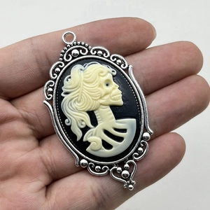 Gothic skull cameo pendant in vintage silver frame held by hand for size reference