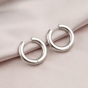 Polished silver titanium steel hoop earrings displayed on soft pink silk fabric