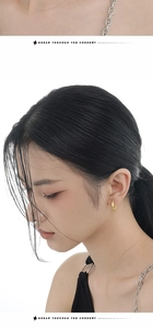 Close-up of textured golden hoop earrings and silver chain necklace worn by a model