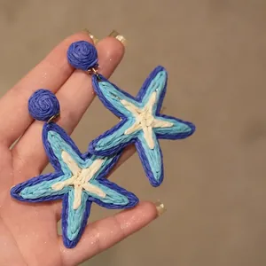 Close-up of bohemian star-shaped woven raffia earrings in blue and beige tones