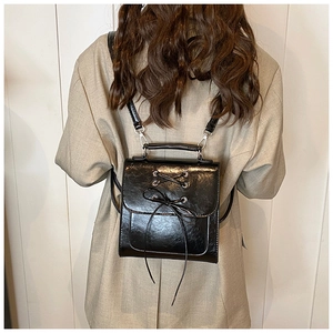 Detail of black glossy PU leather backpack featuring lace-up bow and metal eyelets