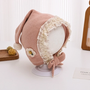 Detail of baby knit hat with lace trim, handmade flower and warm plush pompom