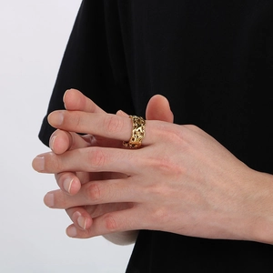 Close-up of a wide gold X-shaped hollow ring with geometric patterns on a male hand