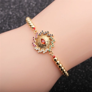 Bracelet à perles dorées avec pendentif œil maléfique en zircon coloré porté au poignet