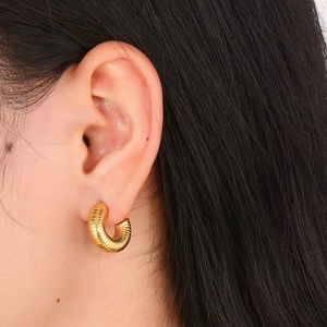 Vue détaillée de boucles d'oreilles créoles dorées en C avec texture nervurée sur l'oreille